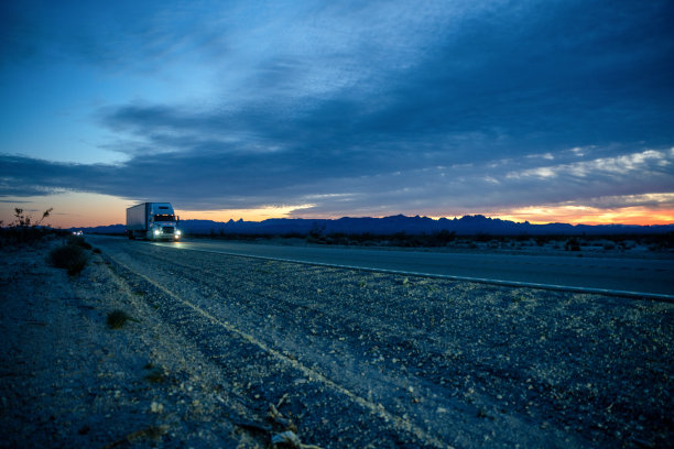 一辆半挂车行驶在两车道的公路上，夕阳下有美丽的云彩图片下载