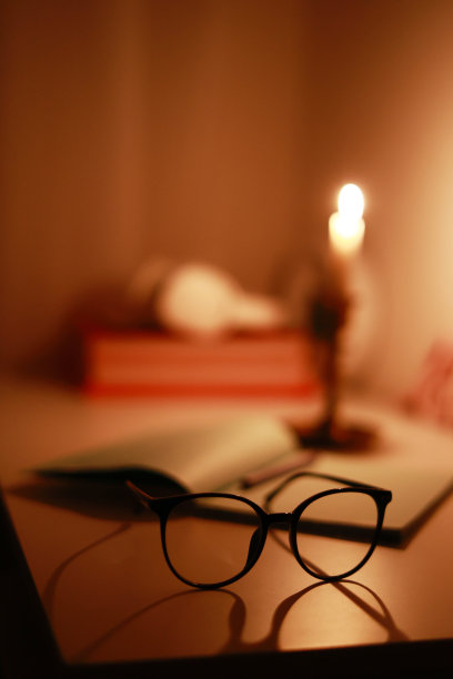 在黑暗的房间里，烛台上燃烧的蜡烛照亮了办公桌上的纸笔记本和笔和眼镜。停电时在家学习和工作。电力问题图片下载