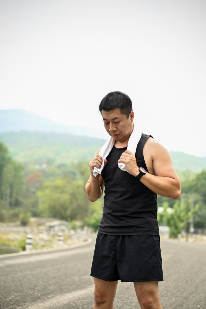 疲惫的成熟亚洲男子穿着运动服，在公园跑步后用毛巾休息。图片下载
