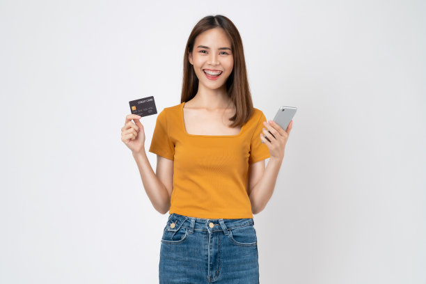 开朗的年轻亚洲女子拿着智能手机，上面有白色背景的模拟信用卡。图片下载