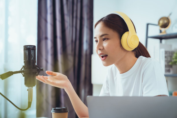 年轻的亚洲妇女使用麦克风，戴着耳机，用笔记本电脑录制播客采访电台。内容创造者概念。图片下载