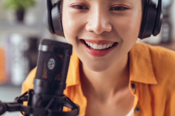 年轻的亚洲妇女使用麦克风，戴着耳机，用笔记本电脑录制播客采访电台。内容创造者概念。图片下载