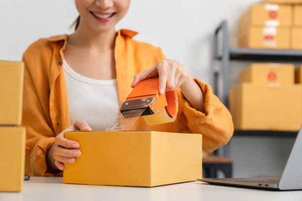 创业小生意，年轻的亚洲女老板使用胶带，包装纸箱包裹盒在家庭办公室工作，卖家准备送货。图片下载