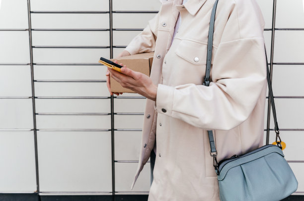 一位女士在自助邮件终端机旁拿着电话。包裹投递机。拿着纸板箱的人。邮件投递和邮政服务，网上购物，电子商务的概念图片下载