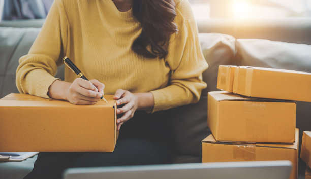 一个独立的亚洲女性使用笔记本电脑和盒子的特写。开朗成功的网络营销包装盒和发送中小企业的概念图片下载