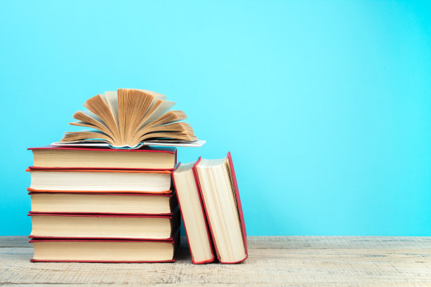 构图与精装书，扇页在木制甲板桌和蓝色背景。书堆积。回到学校。副本的空间。教育背景。图片下载