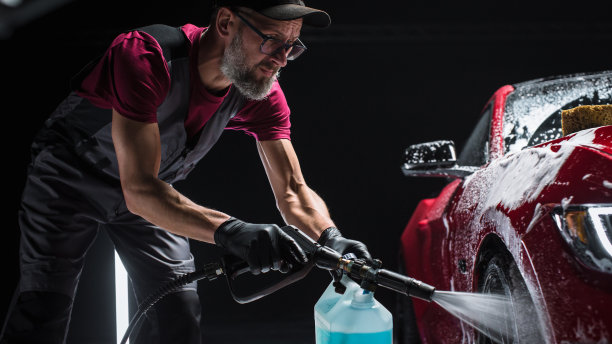 专业洗车工人应用智能泡沫的前轮与复古设计的红色跑车在经销商汽车细节中心。汽车广告商业工作室照片图片下载