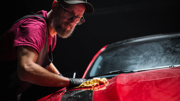 洗车专家用超细纤维布擦干一辆红色现代跑车。成年男子清理污垢，准备美国肌肉车的细节。创意电影照片与跑车图片下载