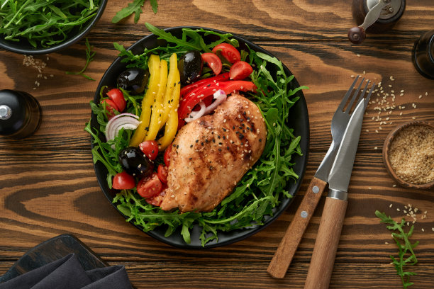 沙拉与烤鸡柳与新鲜芝麻菜，西红柿和橄榄在黑色盘子在旧木制深色背景。鸡肉配沙拉。生酮午餐。健康食品。前视图。图片下载