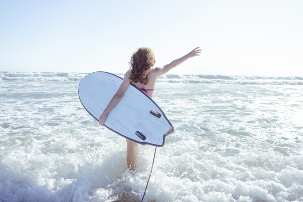 女冲浪者进入水中，手里拿着冲浪板。日落时分在西班牙海洋冲浪。图片下载
