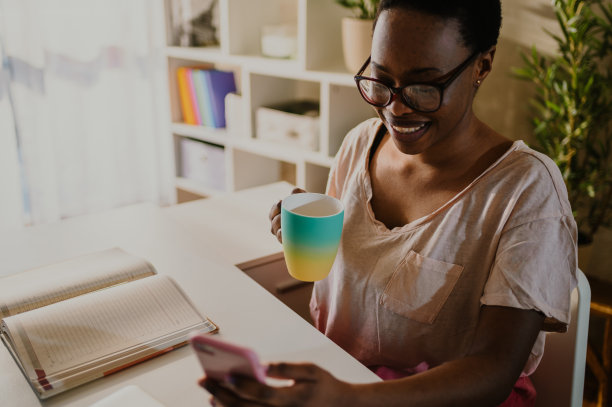 一个非裔美国女性在家里用智能手机喝咖啡的照片图片下载