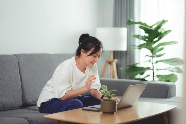 亚洲女性坐在家里的客厅里用笔记本电脑工作。图片下载