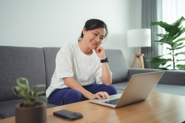 亚洲女性坐在家里的客厅里用笔记本电脑工作。图片下载