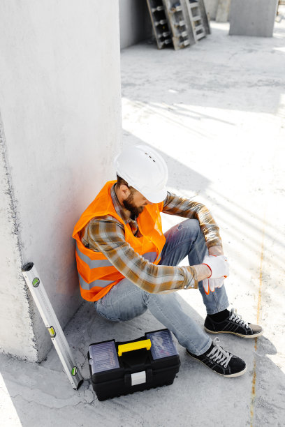 建筑修理工、头戴安全帽和背心的领班在工作场所坐在工具箱和尺子旁边休息图片下载