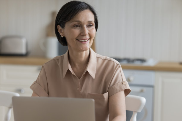 快乐沉思的老年笔记本电脑用户坐在餐桌旁图片下载