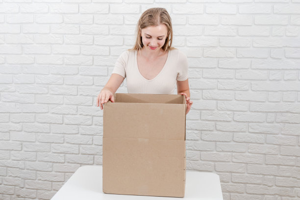 漂亮的金发女人拿着打开的纸板箱。投递包裹图片下载