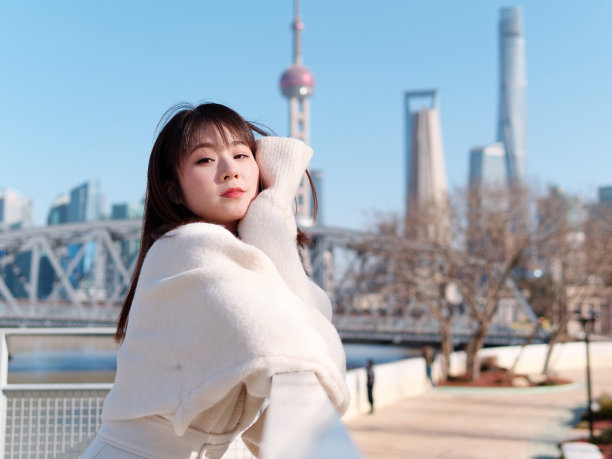 美丽的年轻女子与黑色长发在白色裙子微笑与上海城市外滩地标背景在阳光明媚的日子。情感、人、美、旅行、生活理念。图片下载