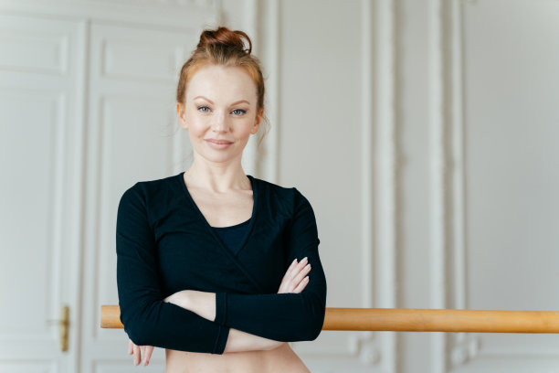 心满意足自信的芭蕾舞者的腰部照片双手交叉在胸前，穿着黑色上衣，留着姜黄色的头发，站在栏杆旁，独自在健身中心摆姿势，使用编舞机图片下载
