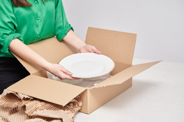 妇女在家里收拾搬家箱。不认识的女人从盒子里取出盘子。图片下载