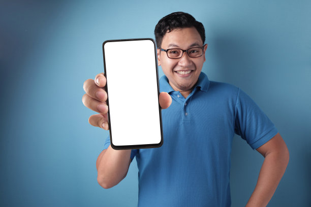 亚洲男子看着镜头，微笑着，展示着空白空白的空白空间手机模拟模板图片下载