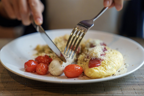 一名年轻女子坐在桌子旁，吃着早餐，有煎蛋、香肠和烤圣女果，为美好的一天奠定了基础图片下载