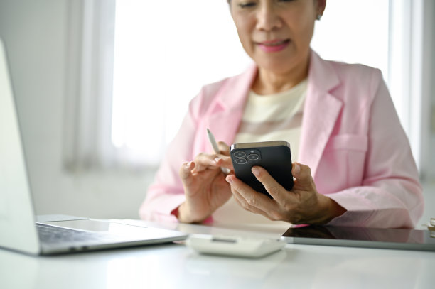 一位资深亚洲女商人在办公桌前使用智能手机的特写。图片下载