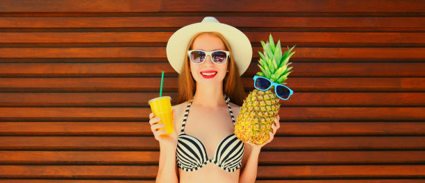 夏日肖像的快乐微笑的年轻女子与菠萝和新鲜的果汁杯戴夏季草帽在木制背景图片下载