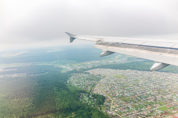 飞机机翼的视图，蓝天和绿色的土地在着陆。飞机窗口视图。图片下载