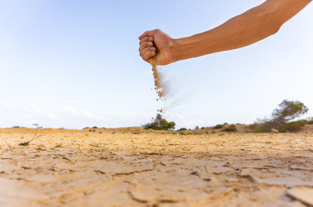 一只手在干燥的土地上撒沙子。图片下载