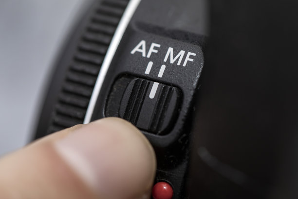 手指在专业相机镜头上选择MF手动对焦模式。有人在镜头照片上设置MF手动对焦模式。相机镜头上的手动对焦MF开关在特写中选择男士图片下载