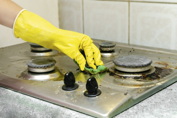 清理煤气灶脏污中的油脂、食物残渣等沉积物。妇女的手戴着防护手套，用海绵抹布和洗涤剂清洗厨房的炉子。家居清洁服务理念图片下载