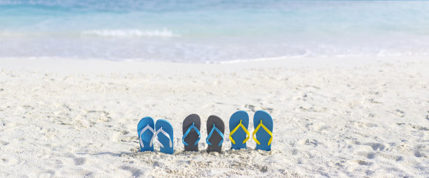 三双人字拖在马尔代夫的海滩上，背景是海洋。家庭度假图片下载