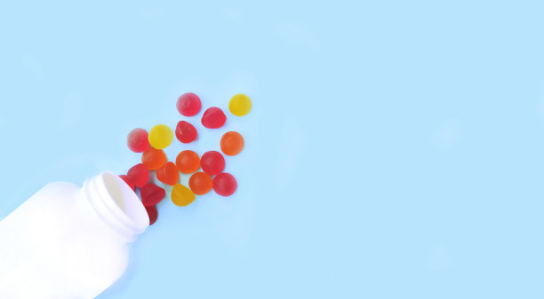 五颜六色的果冻糖，分散在罐子里的维生素，被隔离在蓝色的背景上。图片下载