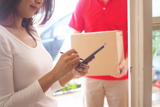 快乐微笑的女人从前门的快递员那里收到盒子包裹。快递员送快递。网购、纸盒、外卖、邮差、快递服务、包裹图片下载