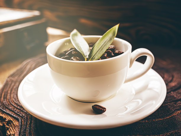 白色的咖啡杯，上面有咖啡豆和绿叶，木制的背景，在早晨的阳光下。木盒子。图片下载