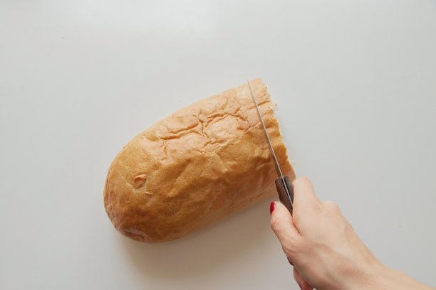 厨房里白色的桌子上，一位女士用刀切着一块面包图片下载