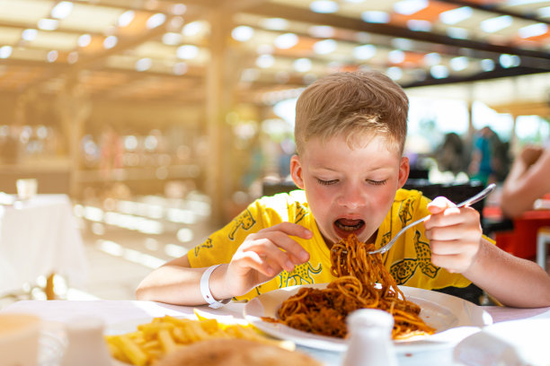 这个男孩正在一家咖啡馆吃午饭。孩子吃意大利面图片下载