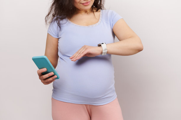 孕妇检查她的智能手表，计算婴儿的运动，在新的怀孕手机应用程序中做笔记图片下载