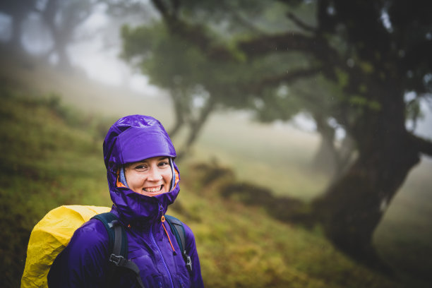 穿着防雨衣服的背包女微笑着看着镜头的侧视图。法纳尔森林，马德拉岛，葡萄牙，欧洲。法纳尔森林，马德拉岛，葡萄牙，欧洲。图片下载