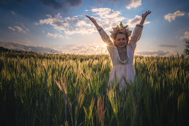 美丽的年轻女孩戴着花冠，穿着保加利亚传统刺绣的民族民俗服装，在夕阳下的麦田里图片下载