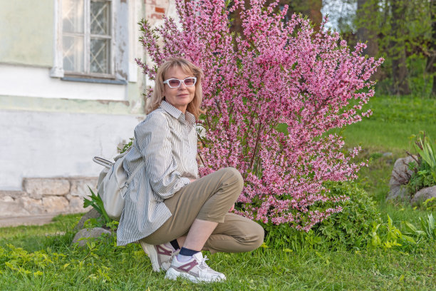 成熟的成年迷人的女人在盛开的灌木草原杏仁与精致的粉红色花朵的背景。图片下载