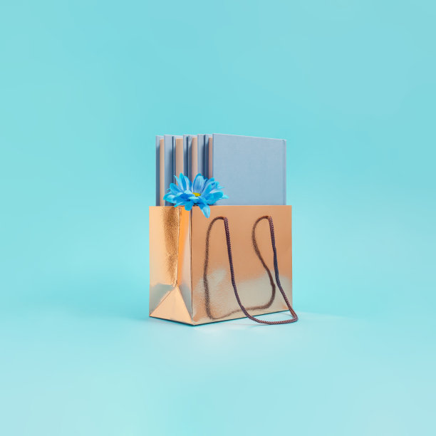 美学组成的淡蓝色的书与鲜花在一个金色的购物袋。概念买卖图书，赠书，教育。图片下载