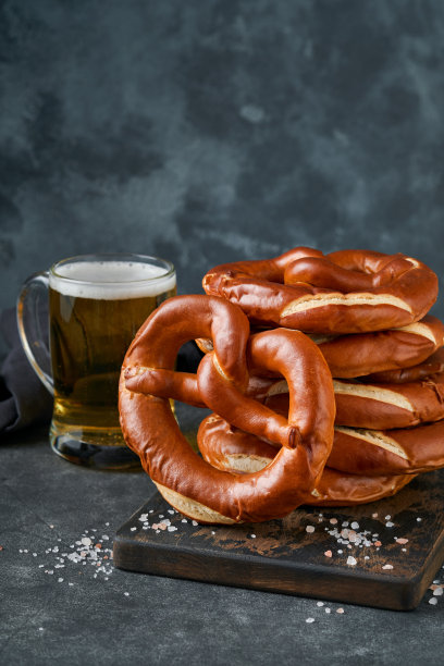 啤酒节概念卡。传统的巴伐利亚椒盐脆饼与啤酒瓶杯在古老的黑色乡村背景。非常适合十月节。啤酒节食物菜单。图片下载