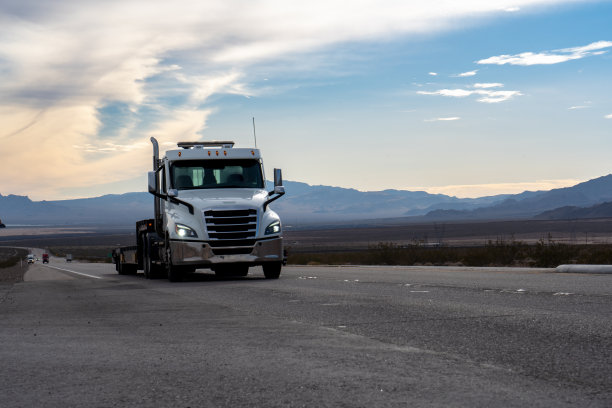 一辆白色的半挂车巡游在内华达沙漠，它巨大的车架与落日的金色形成鲜明的对比。高耸的群山构成了风景如画的背景。图片下载