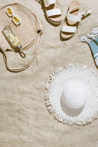 暑假，海滩休息的概念，审美平躺的衣服，沙滩包，白色遮阳帽，皮凉鞋，排毒喝柠檬水沙滩毛巾在阳光下，生活方式时髦的复古照片，顶级图片下载