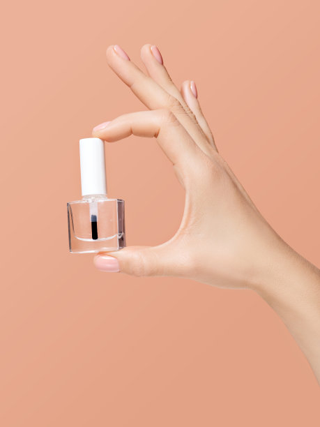 女人手里拿着一瓶干净的指甲油。涂透明清漆。米色背景，居家指甲护理概念。图片为指甲沙龙或美甲师推广。图片下载