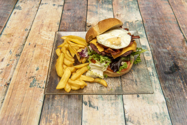 一个玻璃盘子里放着牛肉汉堡，里面有很多生菜芽、切达奶酪、煎蛋和很多培根图片下载