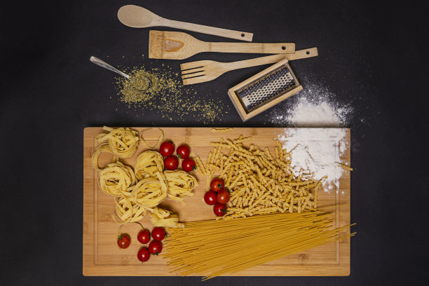 不同类型的意大利生面食，圣女果，小麦粉，厨房用具和勺子与牛至的俯视图图像图片下载