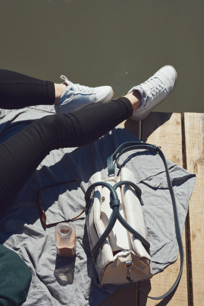 阳光明媚的一天，穿着白色运动鞋的女子在湖边的木甲板上放松。图片下载