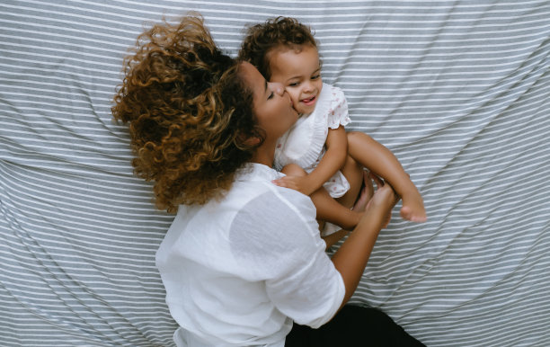 享受在一起的闲暇时光：快乐的年轻非洲裔美国母亲和女儿在床上玩耍亲吻，黑人家庭的假日和团聚，爱的表达。图片下载
